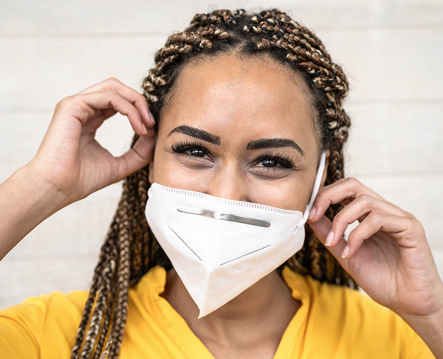 teen girl of color putting on a facemask and wearing scrubs.